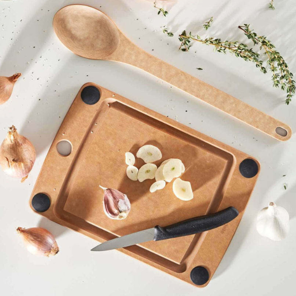 Wooden cutting board with garlic cloves, a knife, and a wooden spoon on a light background.